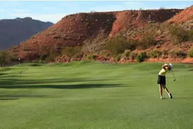 woman playing golf with red hills in the background